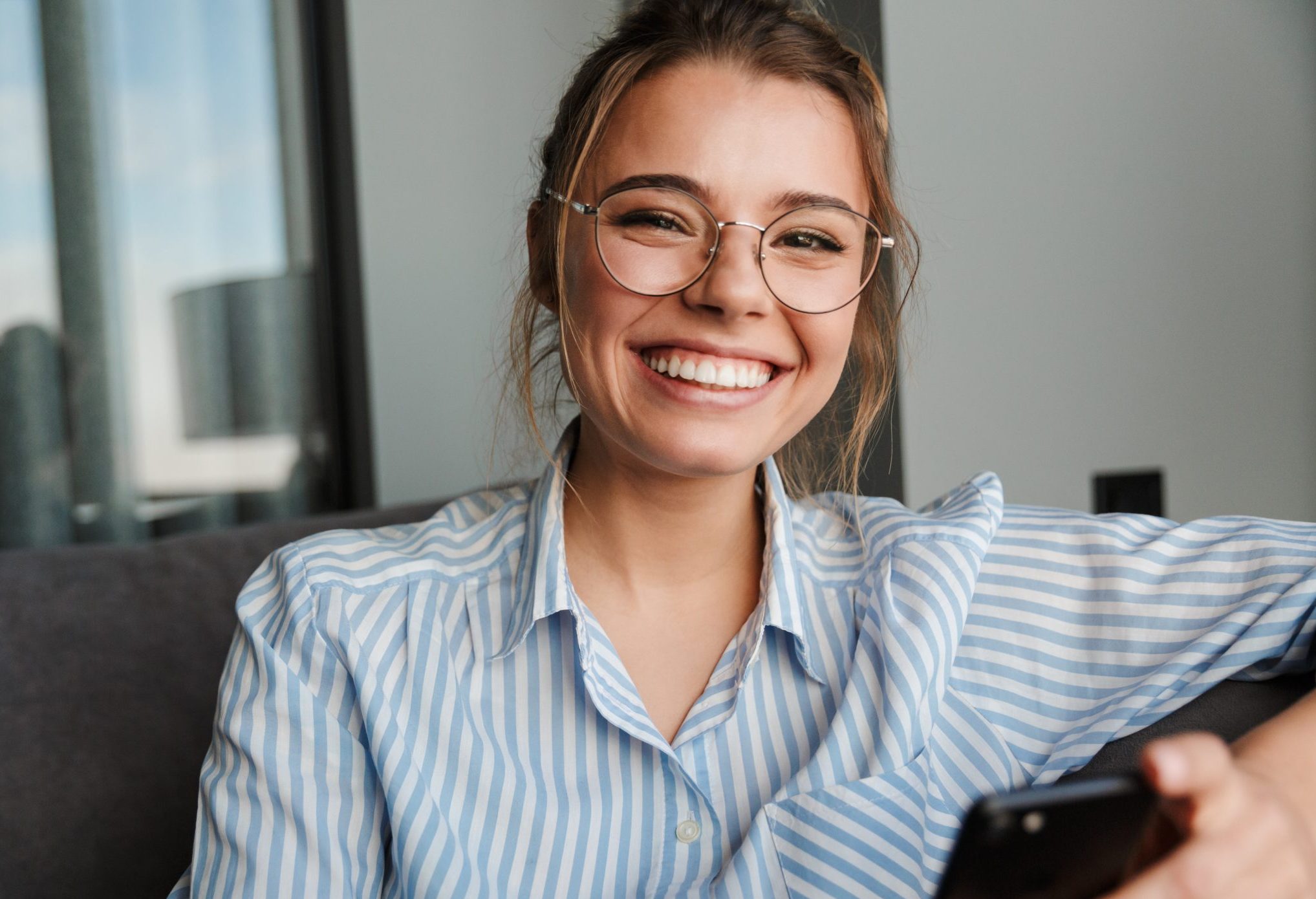 Image of happy young woman in eyeglasses smiling and using cellp