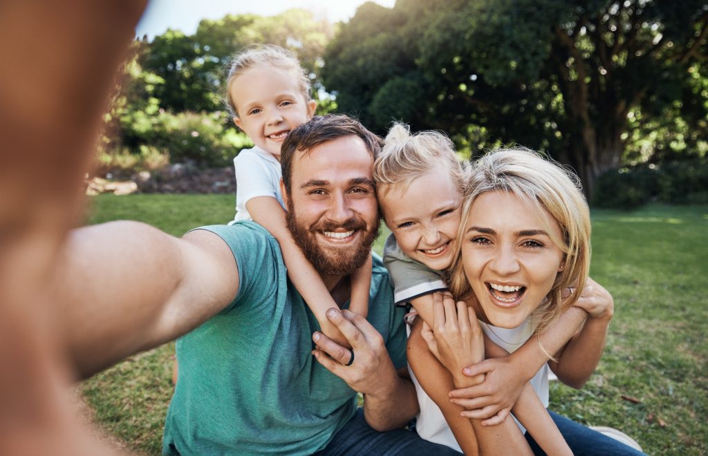 Nature, selfie and portrait of a happy family on a picnic together in outdoor green garden. Happy, smile and parents playing, hugging and bonding with children outside in backyard or park in canada.